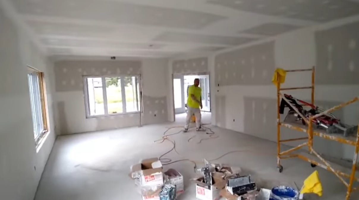 Grande pièce intérieure en construction avec un homme plâtrier qui y travaille Laurent Chainé